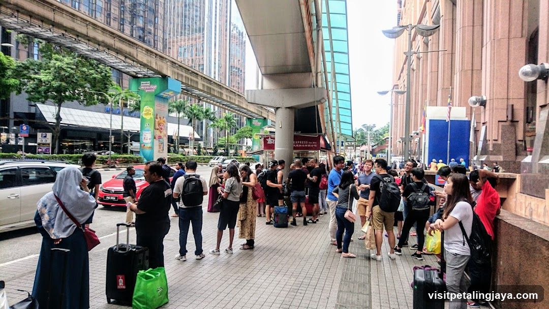 People waiting on a sidewalk under a monorail track
