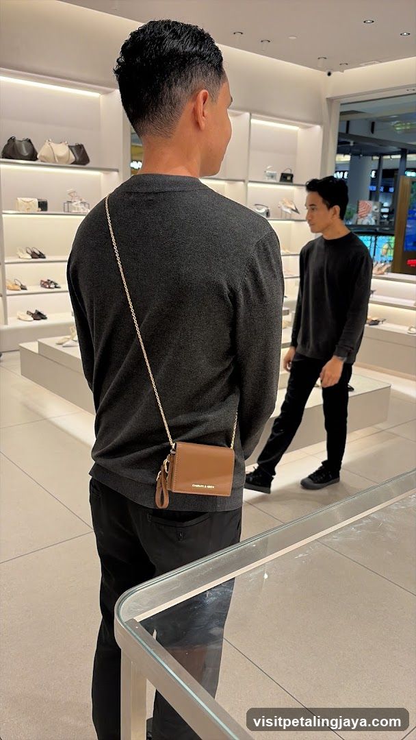 Man wearing a grey sweater and black pants with a brown purse