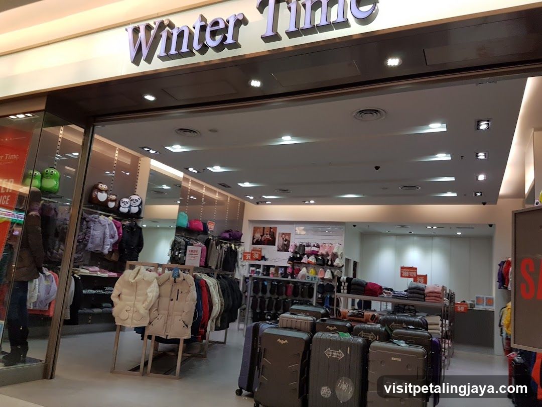 The exterior of a clothing store called Winter Time. The store has a wide entrance and displays clothing on racks and shelves. There are also suitcases visible near the entrance.