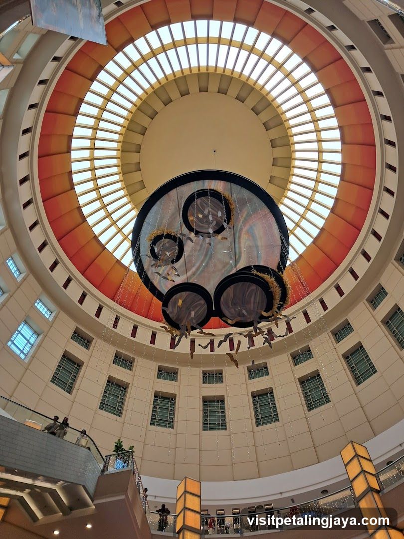 Interior of a circular atrium with a large hanging art installation and a skylight.