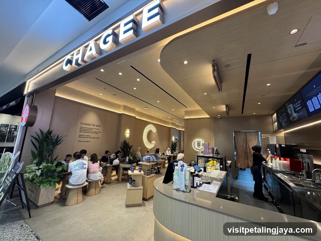 The exterior of a Chagee Tea Bar with prominent signage. The interior shows customers seated at tables and a counter area with staff preparing drinks.