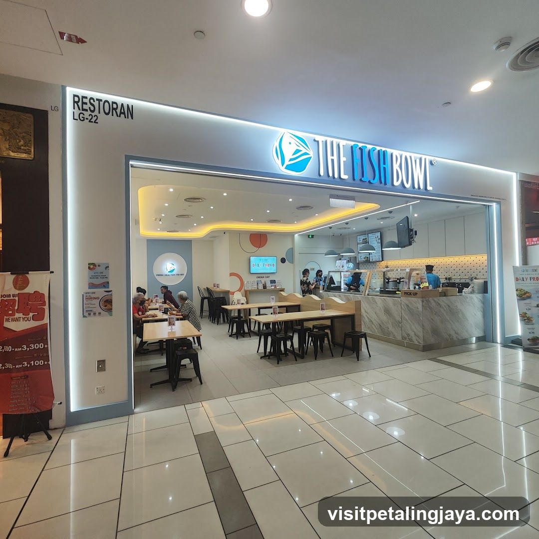 The exterior of a restaurant called The Fish Bowl, with its name and logo prominently displayed above the entrance. Inside, tables and chairs are visible, along with a counter area where staff are working. A promotional poster is displayed to the left of the entrance.