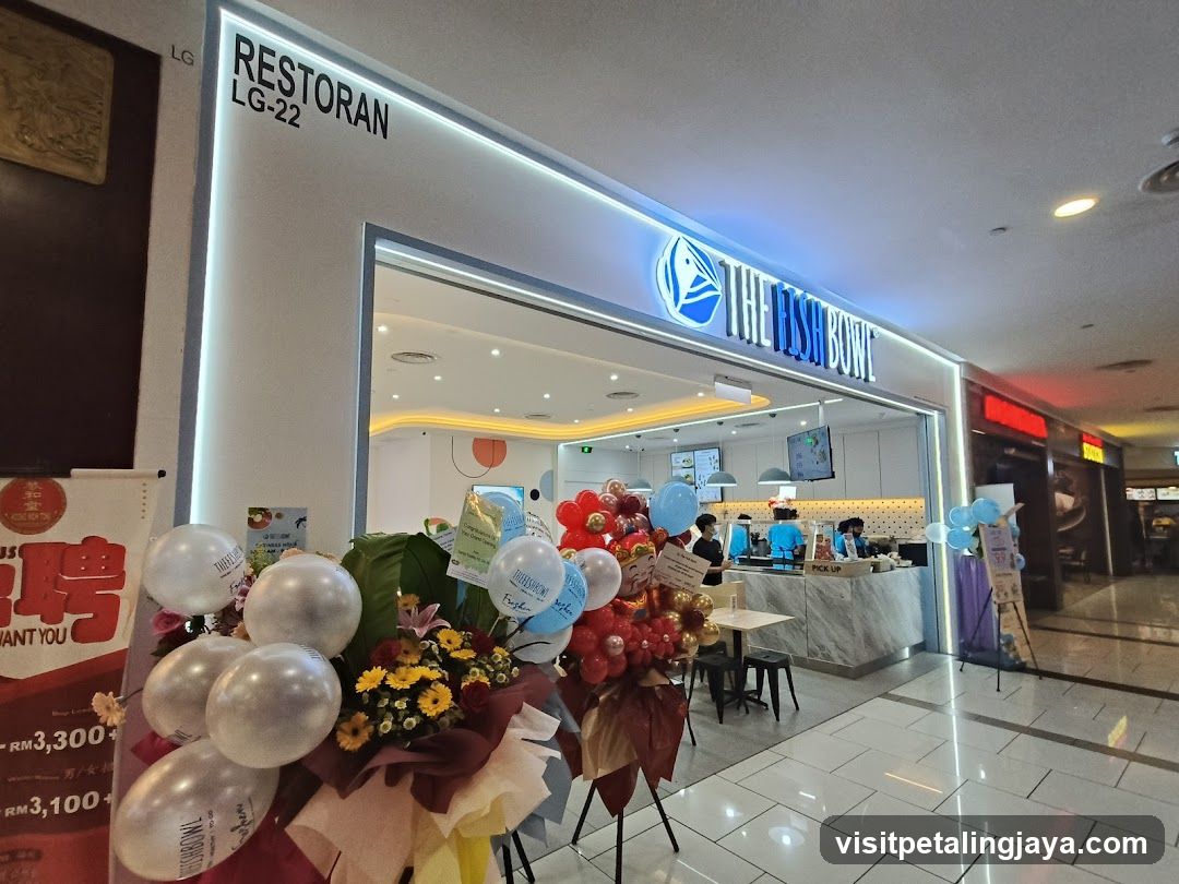 The exterior of a restaurant called "The Fish Bowl" with its name and logo prominently displayed above the entrance. The restaurant appears to be located in a mall, with other shops visible nearby. There are floral arrangements and balloons outside the entrance, suggesting a recent opening or celebration.