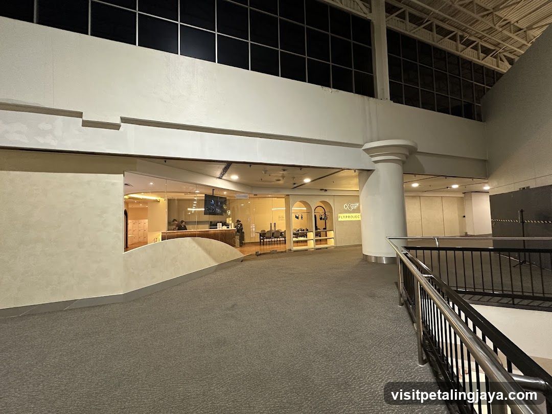 A view of the entrance to a business called Flyproject. The entrance features a glass facade with the company logo and name visible. Inside, a reception desk and lockers can be seen. The area is well-lit with modern lighting fixtures.
