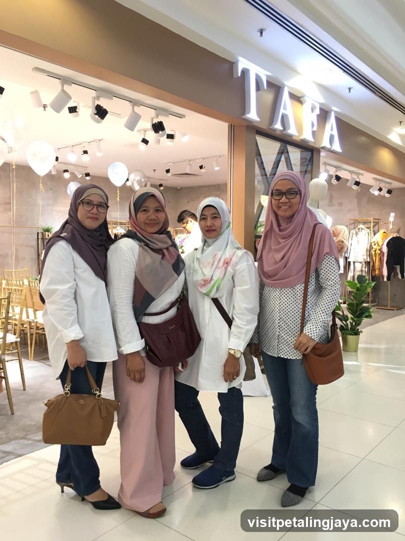 Four women stand in front of a store with the name "TAFA" displayed in large, illuminated letters above the entrance. The store appears to be a clothing boutique, with racks of garments visible inside. The women are dressed in modest attire, with headscarves and long sleeves. The overall impression is one of a clean and modern retail space.