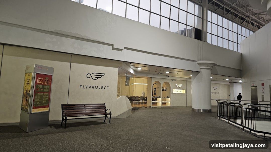The exterior of a Flyproject store with its logo and name visible on the facade. A bench is placed in front of the store. To the left, a display stand shows posters and a menu.