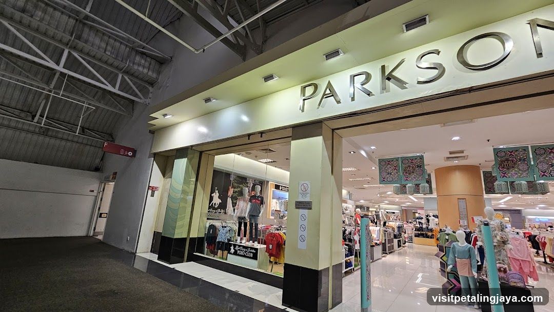 The exterior of a Parkson department store. The large, illuminated sign "PARKSON" is visible above the entrance. The storefront features large glass windows displaying mannequins dressed in clothing. Inside, racks of clothes and more mannequins are visible. Decorative banners hang from the ceiling.