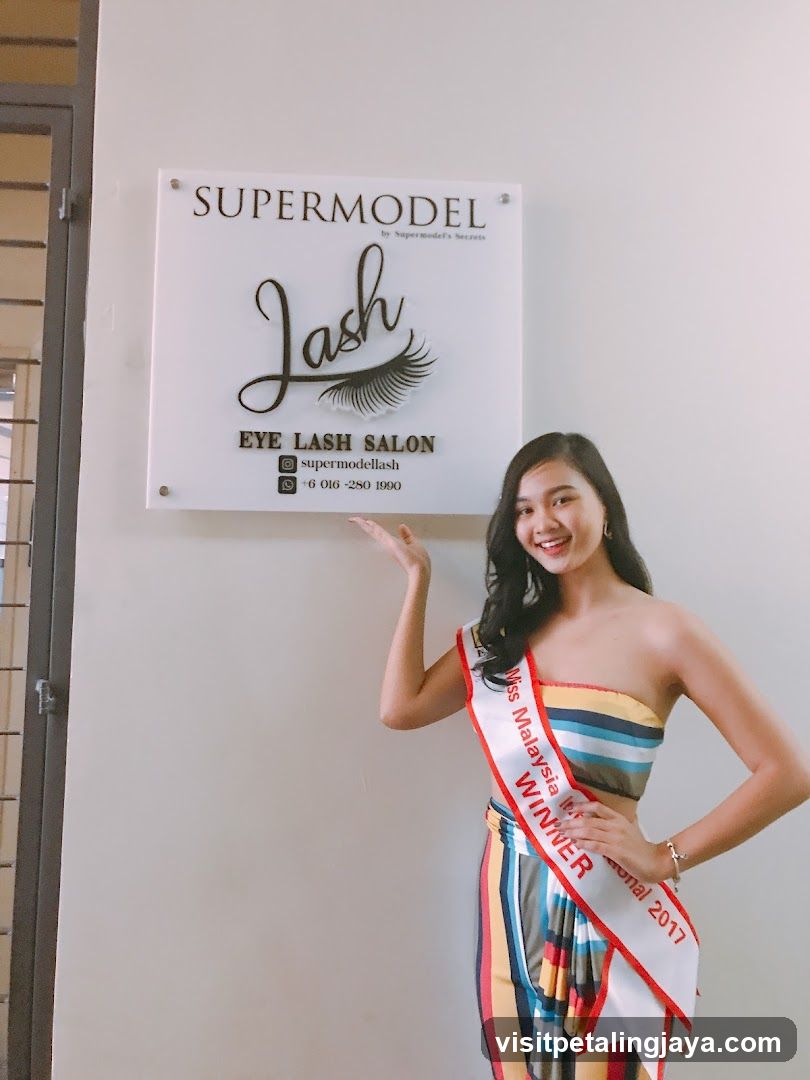 Woman with Miss Malaysia sash in front of lash salon sign