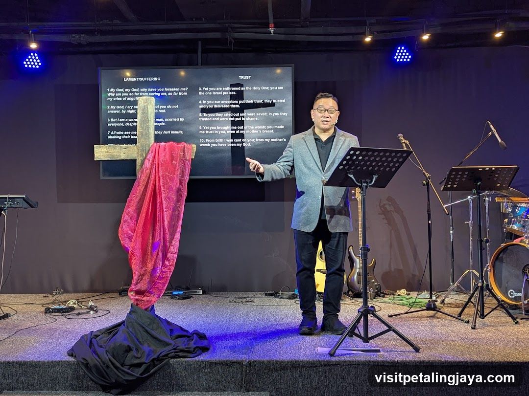 Pastor speaking at a podium with a cross and screen behind him