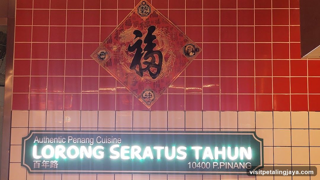 A shop front featuring a red tiled wall with a decorative diamond-shaped sign displaying Chinese characters, including '福' (fortune). Below the tiles is a neon-lit sign reading 'Authentic Penang Cuisine LORONG SERATUS TAHUN 10400 P.PINANG', indicating a restaurant specializing in Peranakan cuisine located in George Town, Penang.