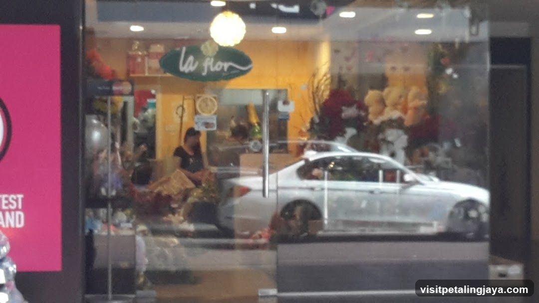 A storefront with a glass facade displaying floral arrangements and decorations inside. A white car is reflected on the window, partially obscuring the view. Inside, there are visible flower bouquets and possibly staff members working.