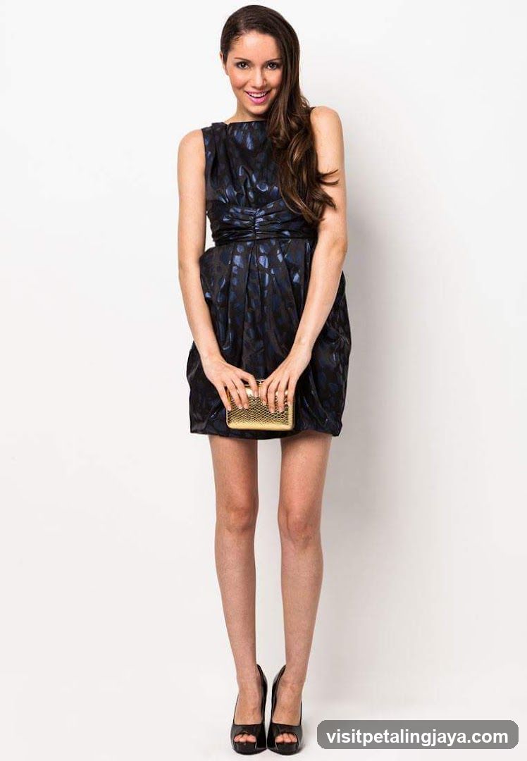 Woman in a dark patterned dress holding a gold clutch