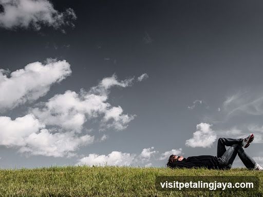 Person Lying on Grass Under Cloudy Sky