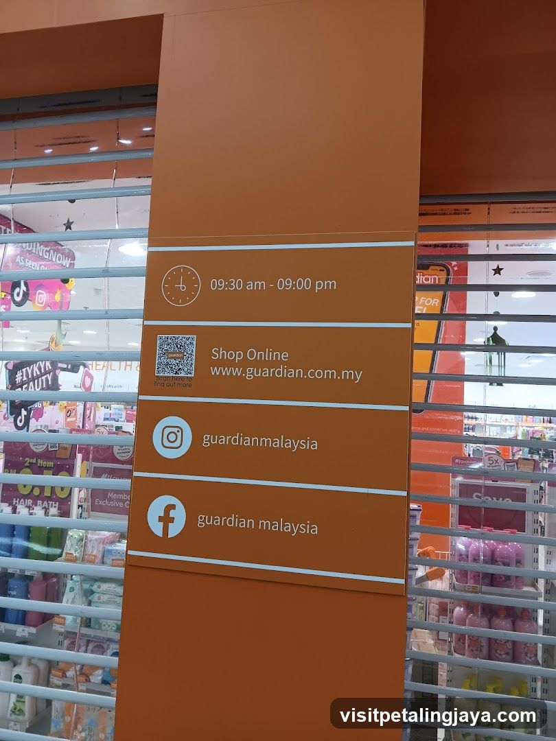 A close-up view of an orange pillar sign outside a store, displaying operating hours (09:30 am - 09:00 pm), a QR code with 'Shop Online' and the website www.guardian.com.my, Instagram handle @guardianmalaysia, and Facebook page guardian malaysia. The background shows glass windows with horizontal blinds reflecting interior shelves stocked with colorful products like hair care items.