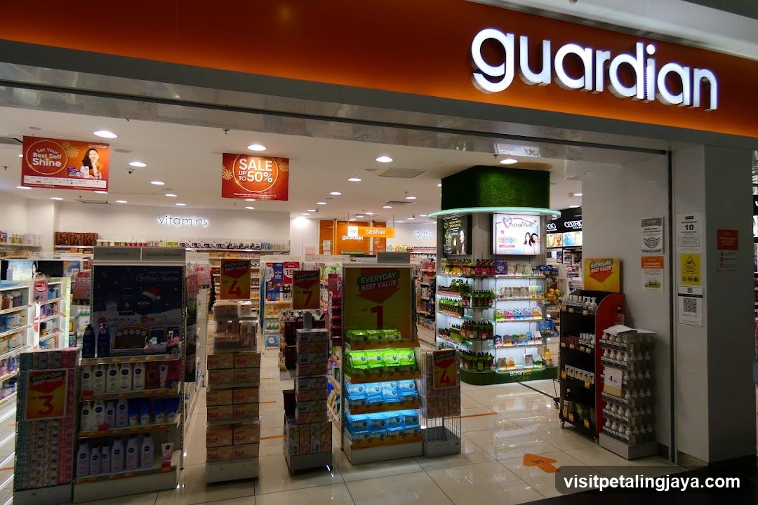 The image shows the storefront of a Guardian store, with its name prominently displayed in white letters on an orange background above the entrance. Inside, there are various product displays and promotional signs indicating sales.