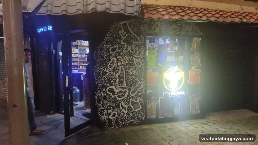 A shop front at night featuring a brightly lit entrance, neon signs, and decorative wall art. The store displays various products inside, including beverages and snacks.