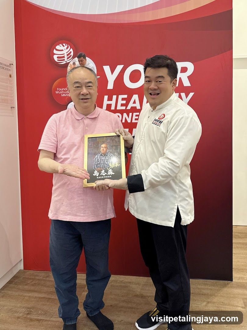 Two men holding a framed photo in front of a red wall with branding