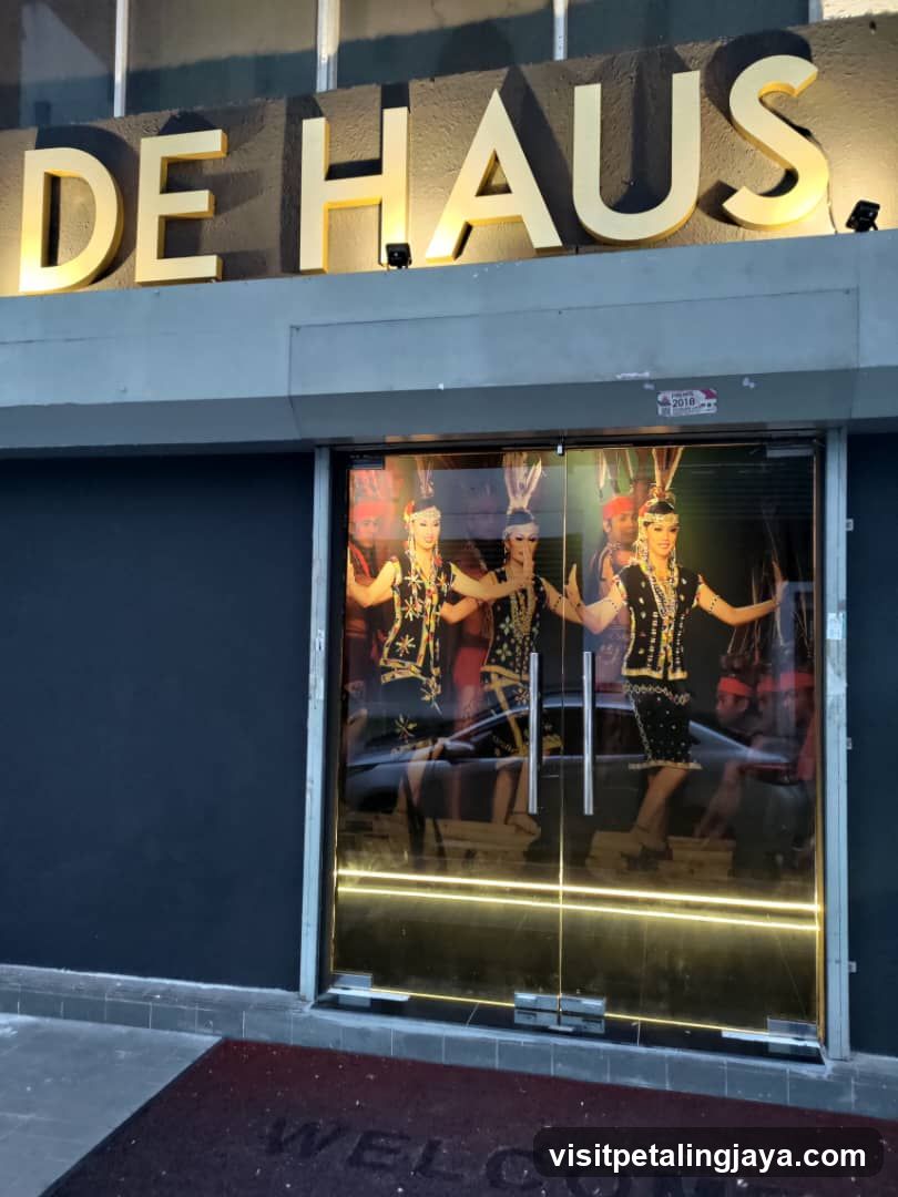 Exterior view of a shop entrance with illuminated signage reading 'DE HAUS' above glass doors. Inside, performers in traditional costumes are visible through the windows.