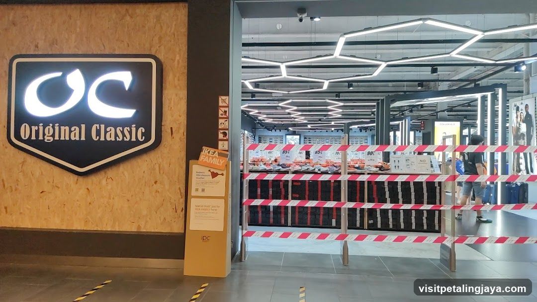 The image shows the entrance of a store named 'Original Classic', with its logo prominently displayed on a wooden wall to the left. The interior is visible through an open doorway, featuring hexagonal ceiling lights and shelves stocked with products. Red and white striped barriers block part of the entrance area.