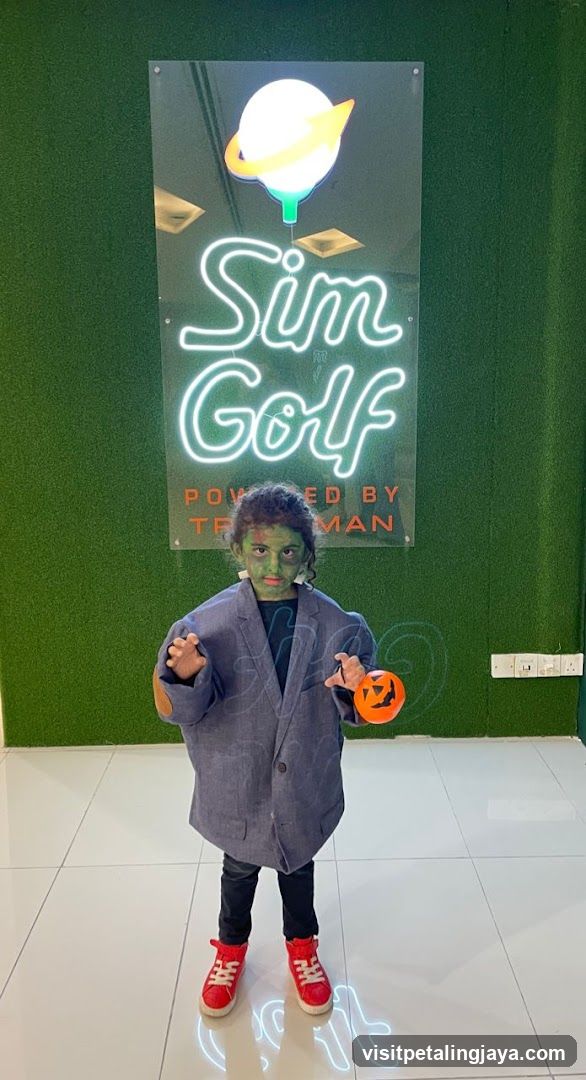 Child in costume posing with Sim Golf sign