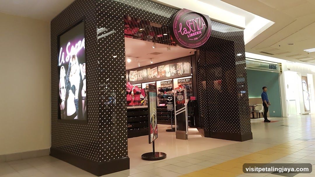 A storefront with a black and white polka dot exterior, featuring a large illuminated sign reading 'La Senza' on the left side. The entrance is open, revealing shelves stocked with various products inside. A circular logo above the entrance displays 'La Senza Lingerie'. Inside, there are racks of clothing and promotional posters.