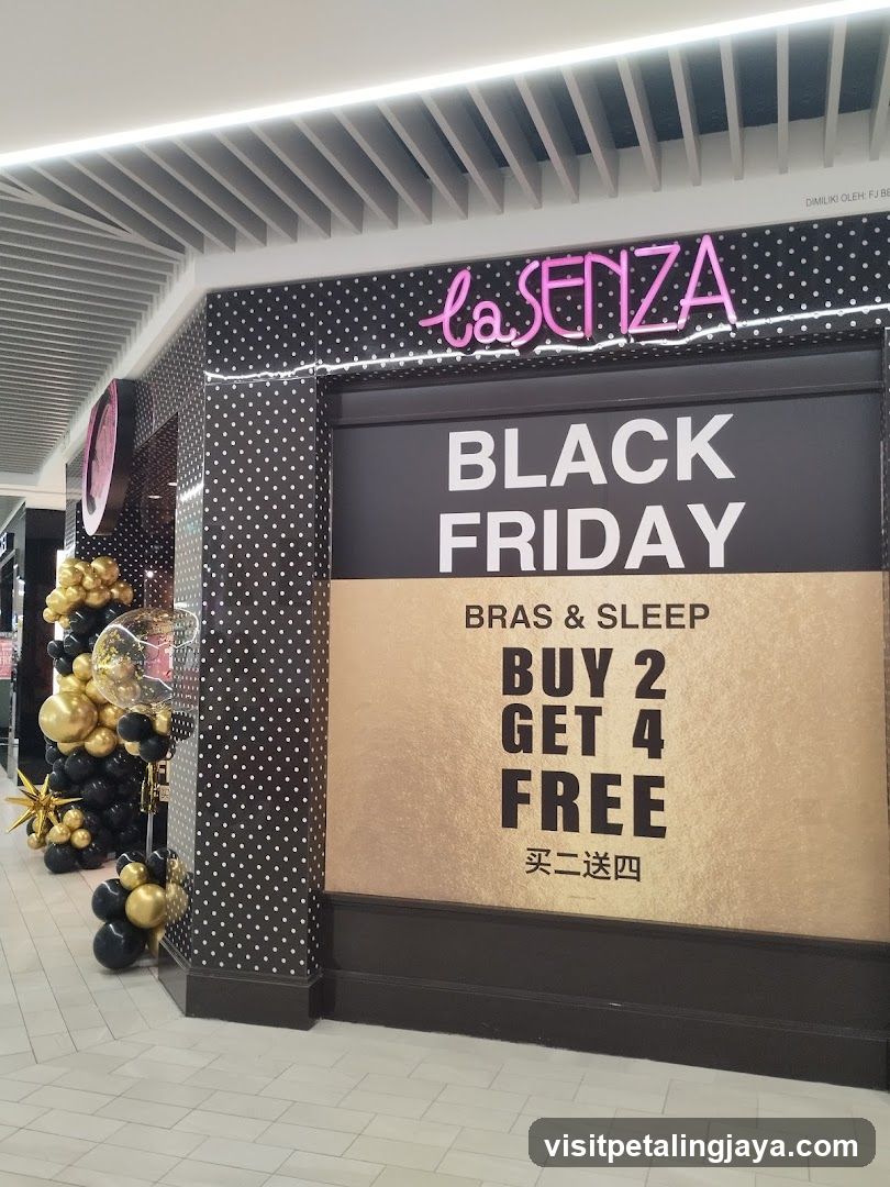 Storefront of La Senza lingerie brand featuring a large promotional sign advertising 'Black Friday' with 'Buy 2 Get 4 Free' on bras and sleepwear. The entrance is decorated with black, gold, and white balloons arranged in clusters near the door frame. The building facade has a polka-dot pattern background behind the signage.