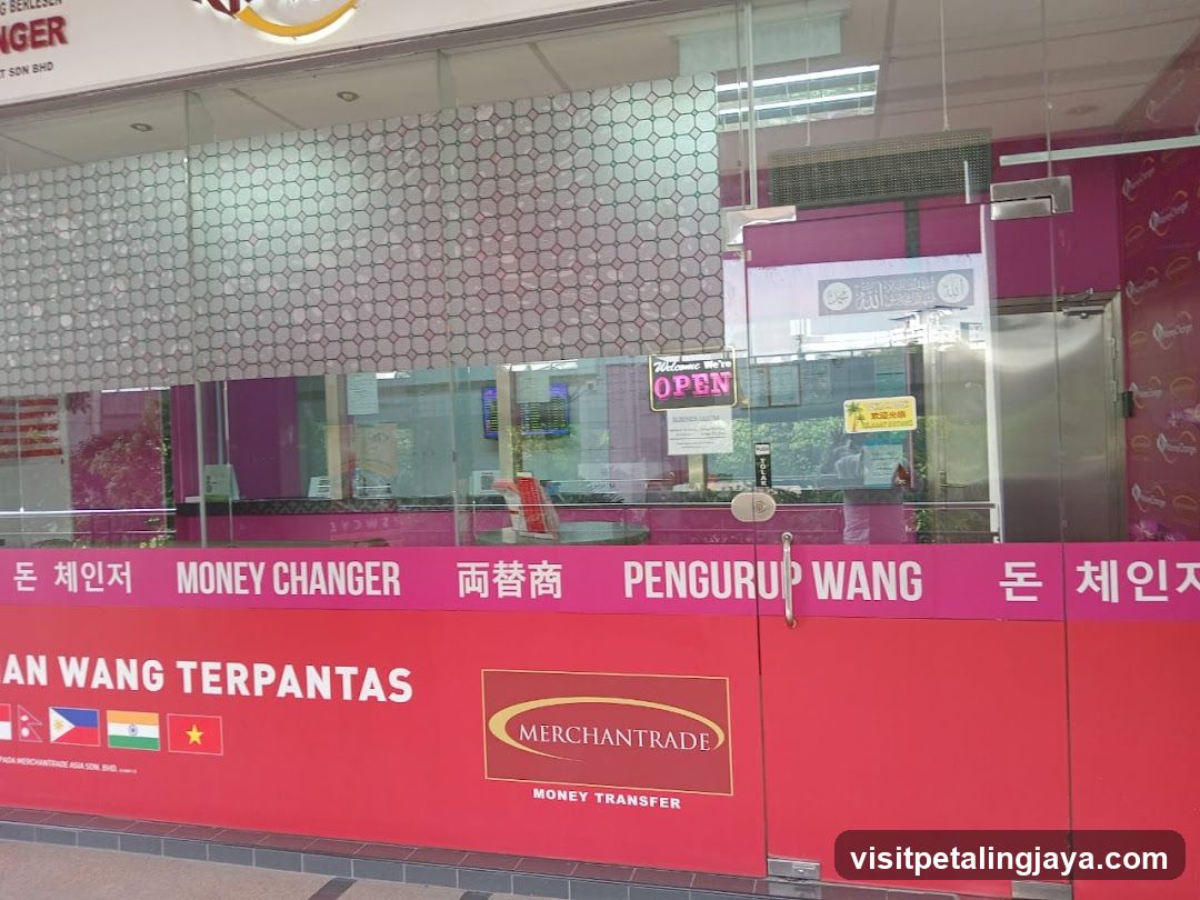 A storefront with a glass facade and pink signage displaying 'MONEY CHANGER' in multiple languages including Korean, Chinese, Malay, and Vietnamese. The sign also includes flags of the Philippines, India, and Vietnam. A logo for 'Merchant Trade Money Transfer' is visible on the lower part of the wall.