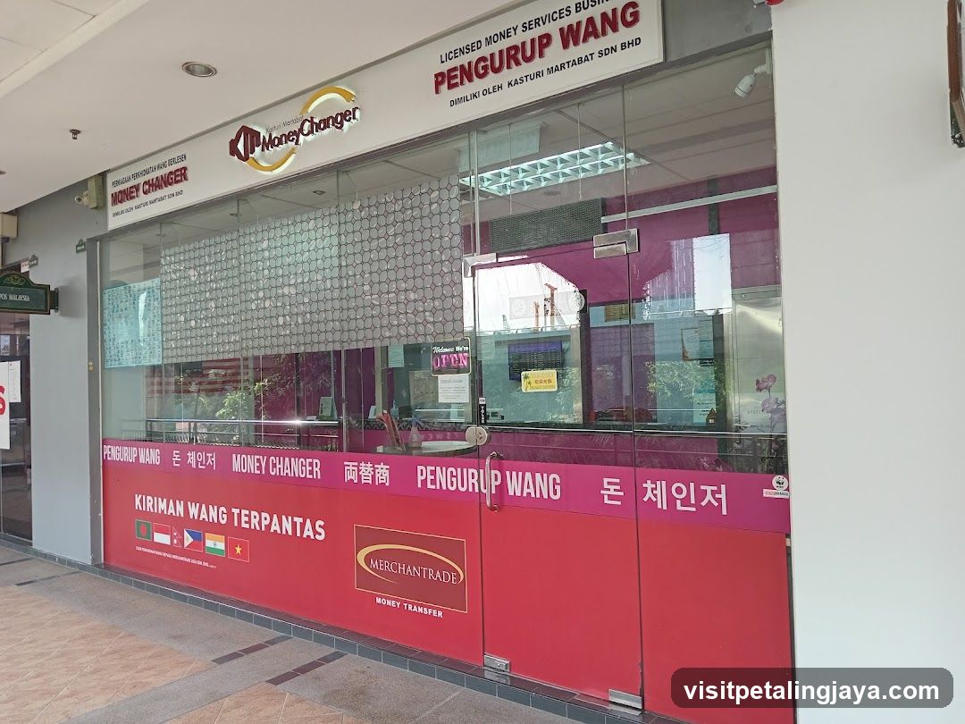 A storefront of a money changer business with visible signage in multiple languages including English, Chinese, and Korean. The shop features glass doors and windows with red branding panels displaying 'Pengiruman Wang Terpantas' and various currency flags.