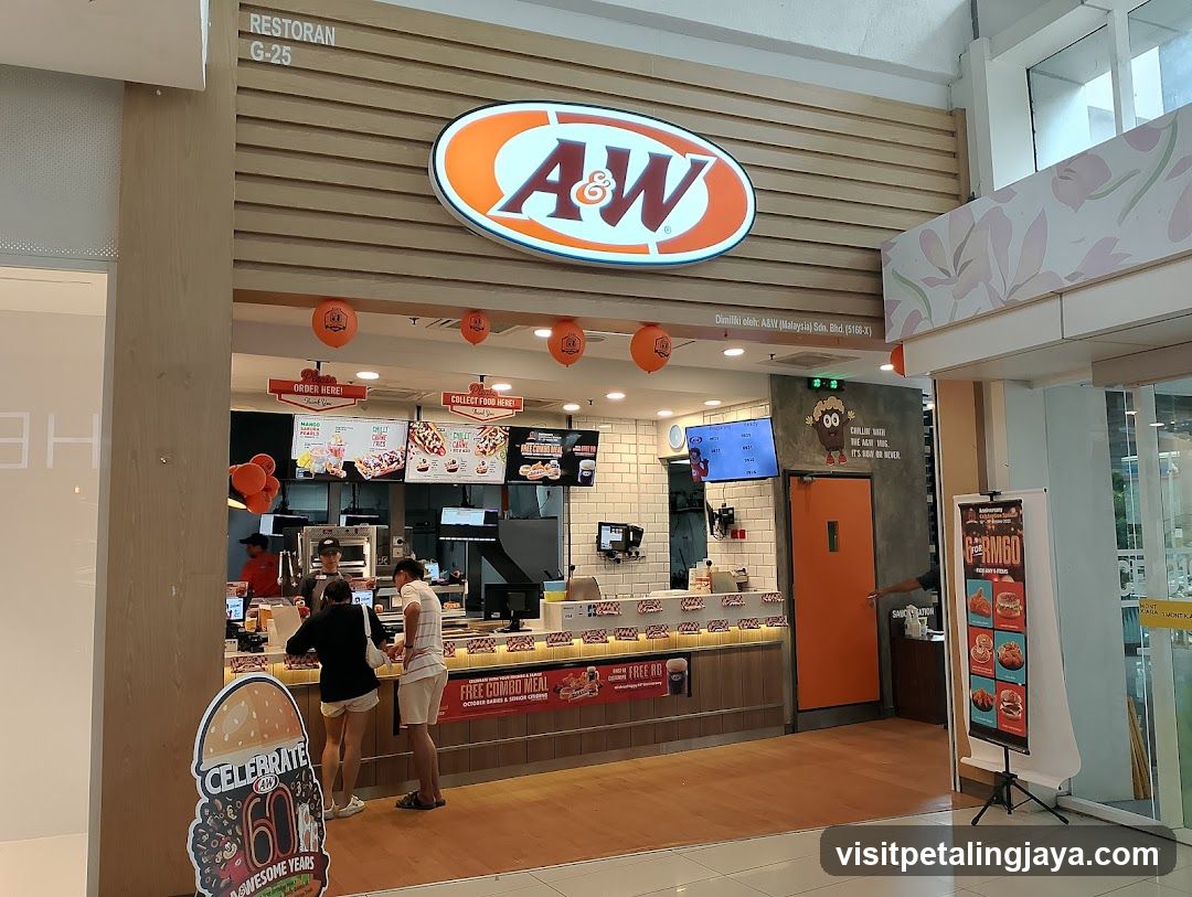 The image shows the storefront of an A&W food outlet, likely within a mall or food court. The shop features a prominent oval logo with 'A&W' in bold letters on a wooden slat facade. Below the counter, there are digital menu boards displaying various food items and prices. There is also a promotional sign celebrating '60 Awesome Years'. Staff members can be seen behind the counter, and customers are standing at the ordering area.