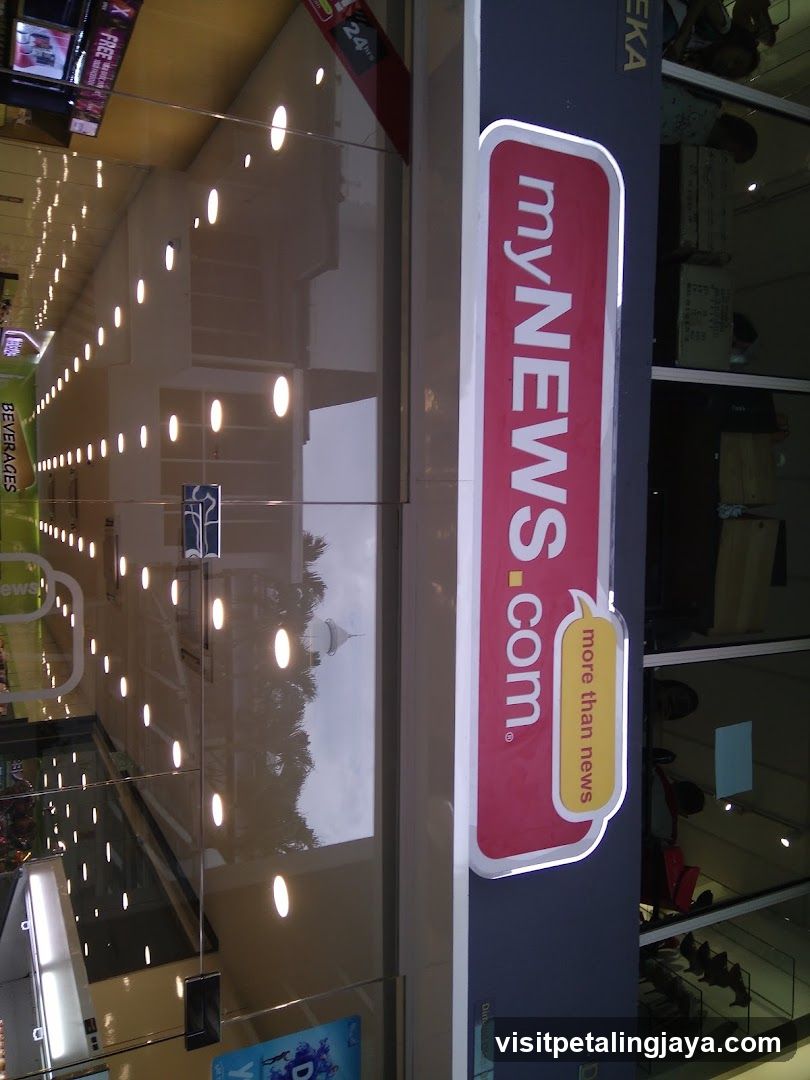 Vertical sign with 'myNEWS.com' logo and tagline 'more than news', mounted on building facade near glass entrance.