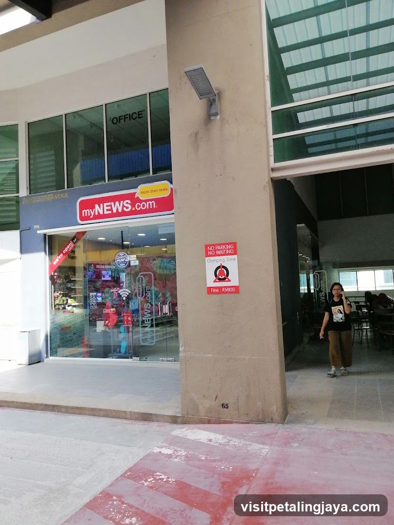 Exterior view of a shop with 'myNEWS.com' signage above the entrance. The building features large glass windows and doors, with visible interior displays including promotional banners and products. A person is standing near the entrance on the right side.