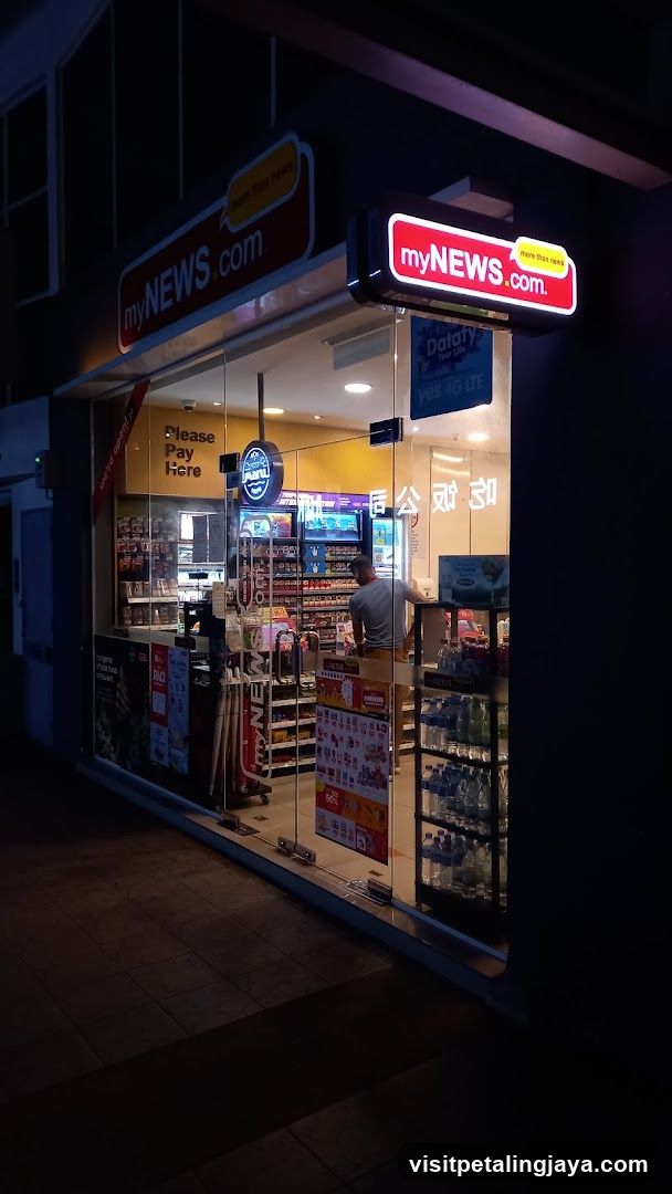 A brightly lit convenience store entrance with 'myNEWS.com' signage above and on the glass door. Inside, shelves stocked with bottled water and snacks are visible through the transparent facade. A person stands near the center aisle. Posters and promotional materials line the interior walls.