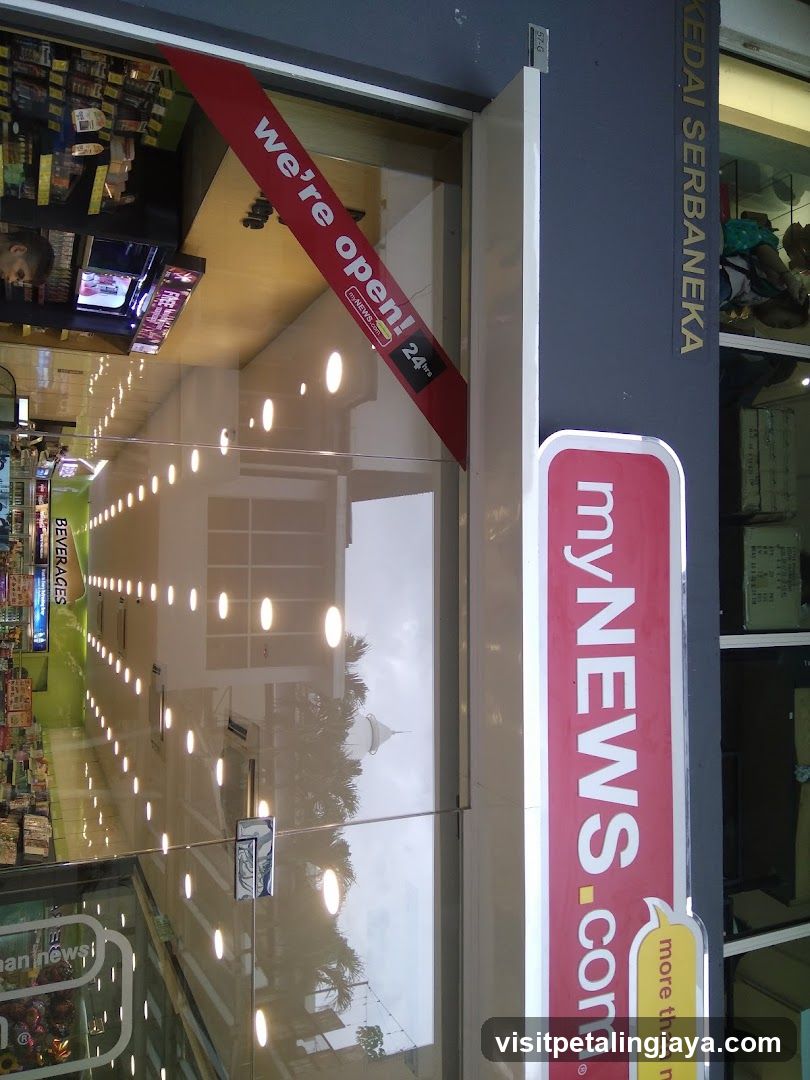 Photo of the exterior entrance to a myNEWS.com store, featuring glass doors with 'we're open!' and '24h' signage. The shop sign is visible on the building facade.