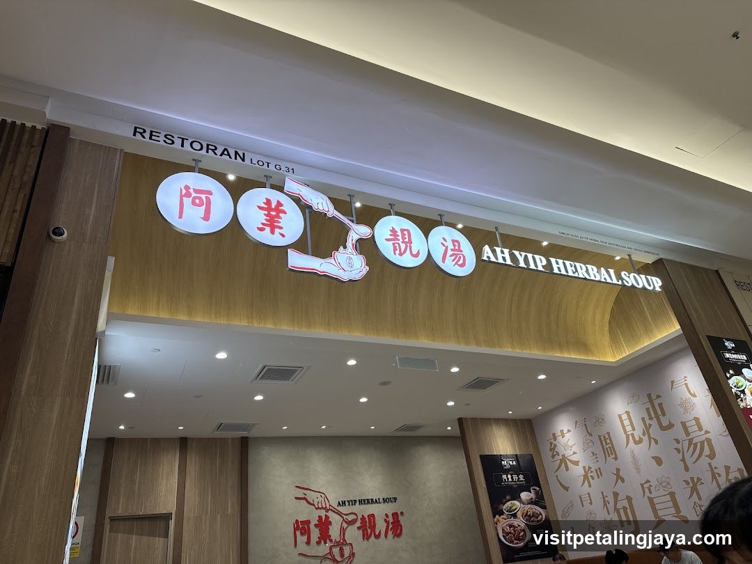 The image shows the storefront of Ah Yip Herbal Soup, featuring a prominent sign with Chinese characters and English text. The entrance is visible with wooden paneling and recessed lighting above.