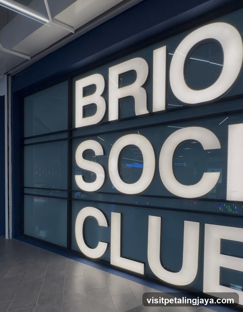 A close-up view of a modern storefront featuring large, illuminated white lettering on a dark blue background. The sign reads 'BRIO SOCIAL CLUB' in bold sans-serif font across three lines. The letters are backlit and mounted within a grid-like frame that appears to be part of the building's facade or window structure. Reflections from interior lights and possibly streetlights can be seen through the glass panels behind the signage. The floor is tiled with light gray square tiles.