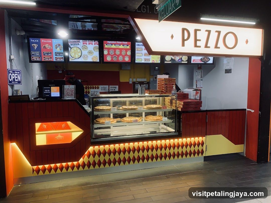 The image shows the storefront of a pizza shop named 'PEZZO'. The sign is prominently displayed above the entrance. There are illuminated menu boards showing various pizza options and prices. A glass display case with pizzas is visible inside the shop. The interior has red and yellow accents, and there's an open sign on the left side.