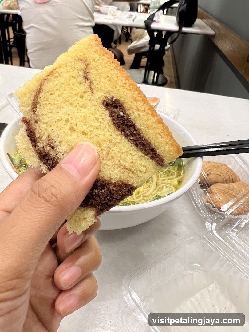 Hand holding cake slice near noodle bowl