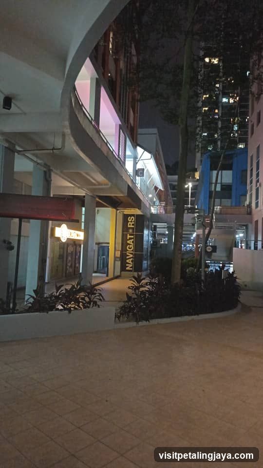 Night scene of a commercial area with illuminated storefronts and signage.