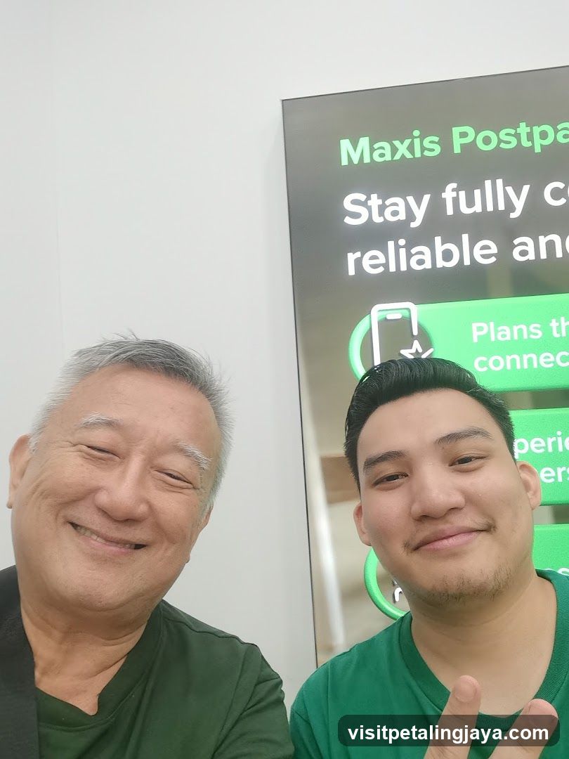 Two men posing in front of a Maxis poster