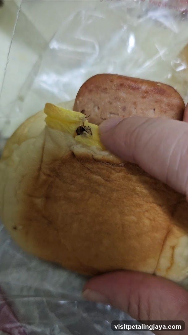 Hand holding a bread roll with sausage and egg