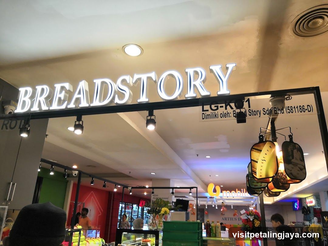 The image shows the exterior entrance of a Breadstore store, with its illuminated sign prominently displayed above the entrance. The store is located in a shopping mall, as indicated by the surrounding environment and other visible shops. There are no menus or price lists visible in the image.
