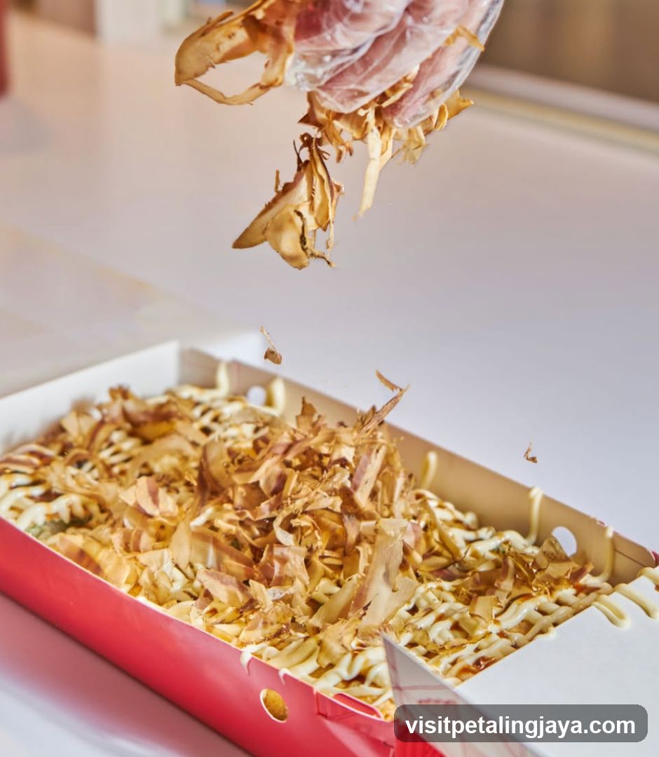 Okonomiyaki with bonito flakes being sprinkled