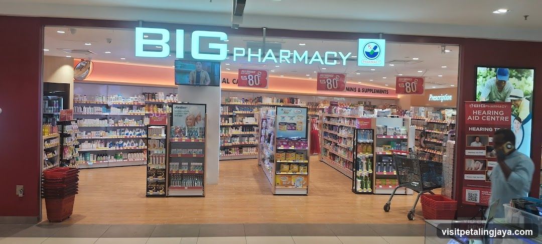 The photo shows the exterior entrance of a Big Pharmacy store, with visible signage above the glass doors and shelves stocked with various products inside.